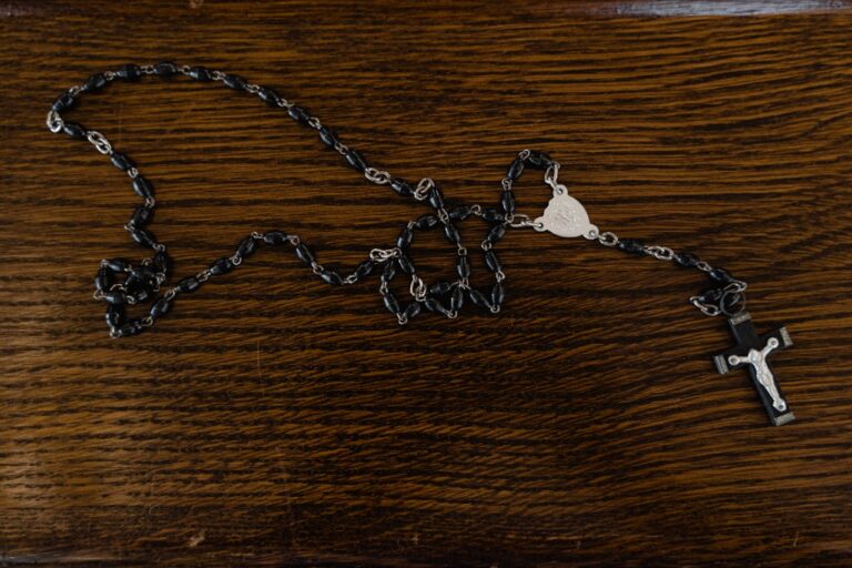 A rosary with black beads and cross on a wooden table.